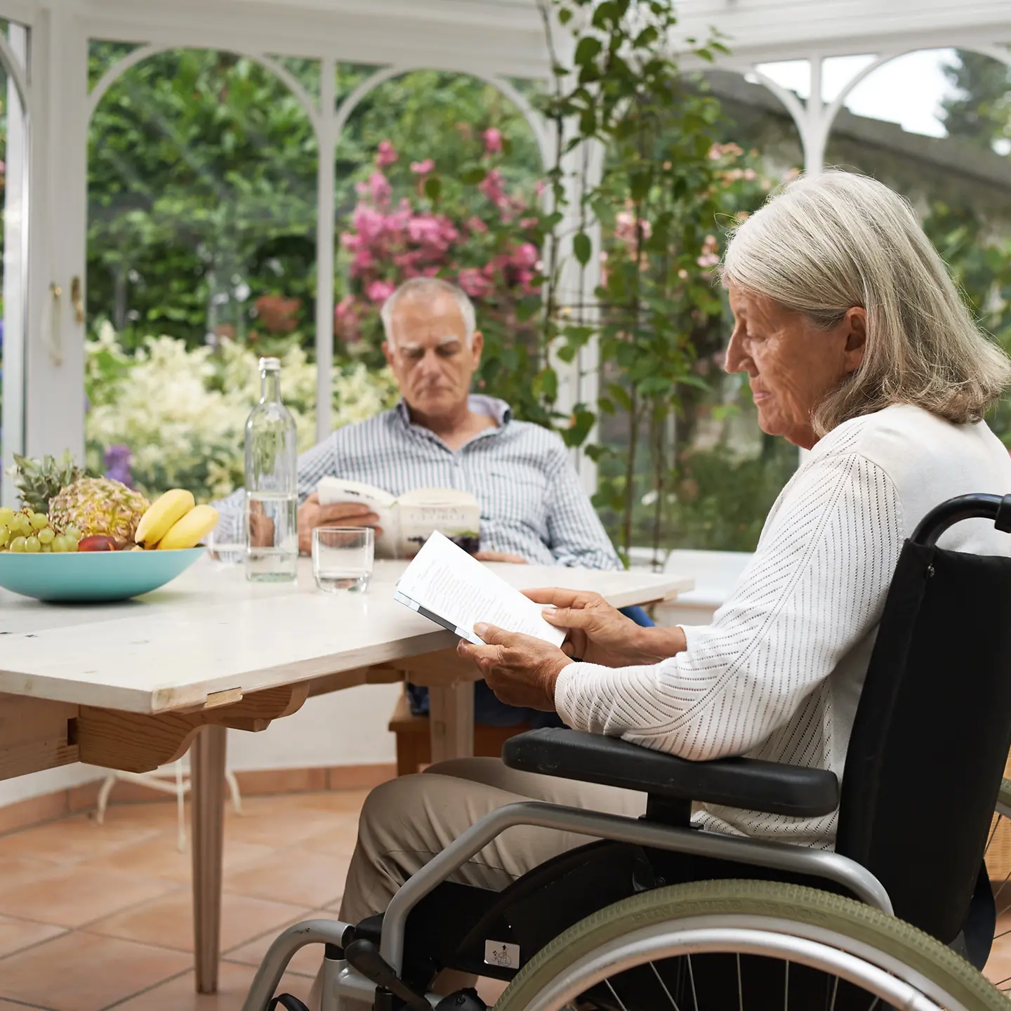 Eine Frau im Rollstuhl wird von einem Mann im häuslichen Umfeld gepflegt