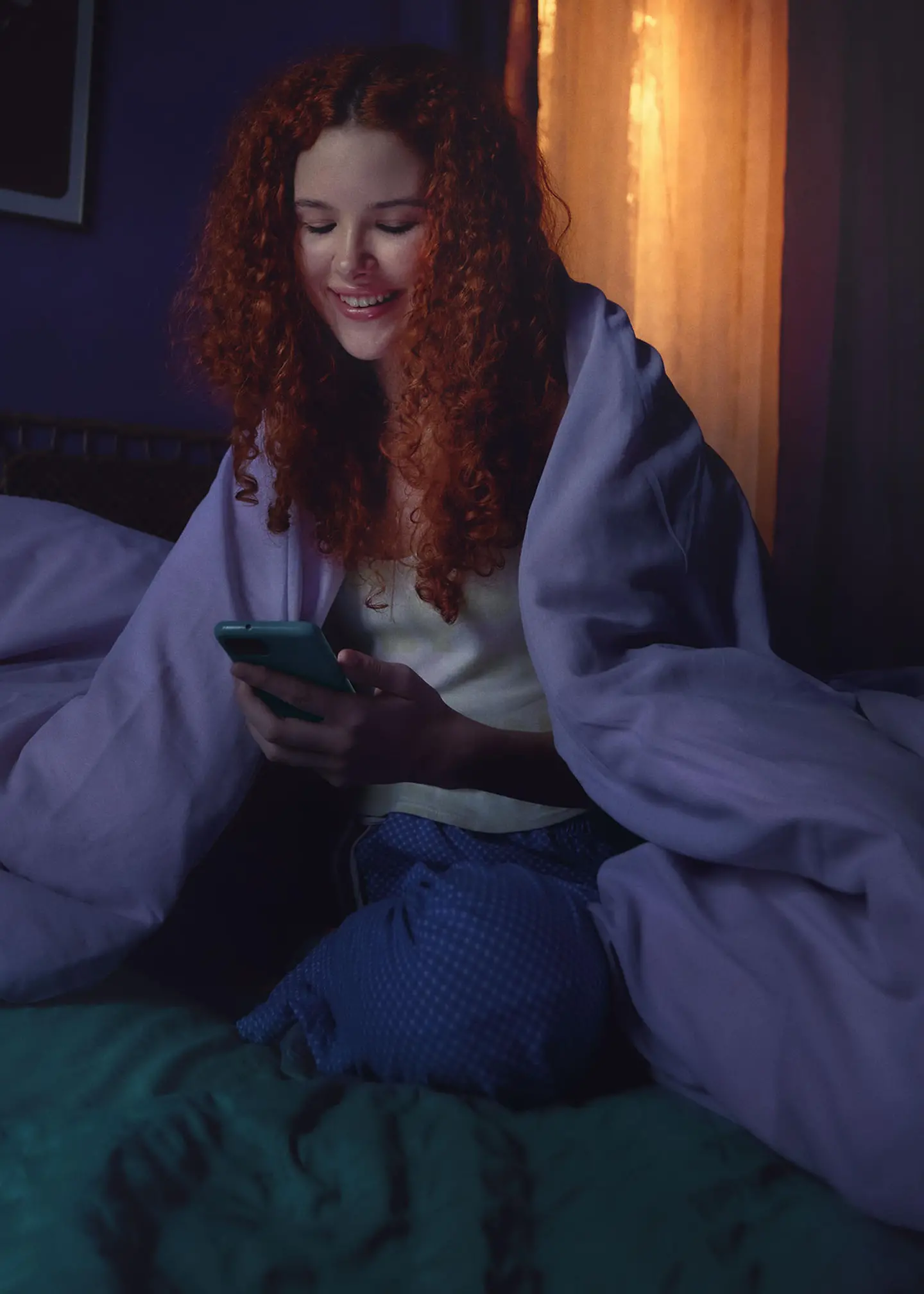 Eine Frau sitzt auf dem Bett und schaut auf ihr Handy.