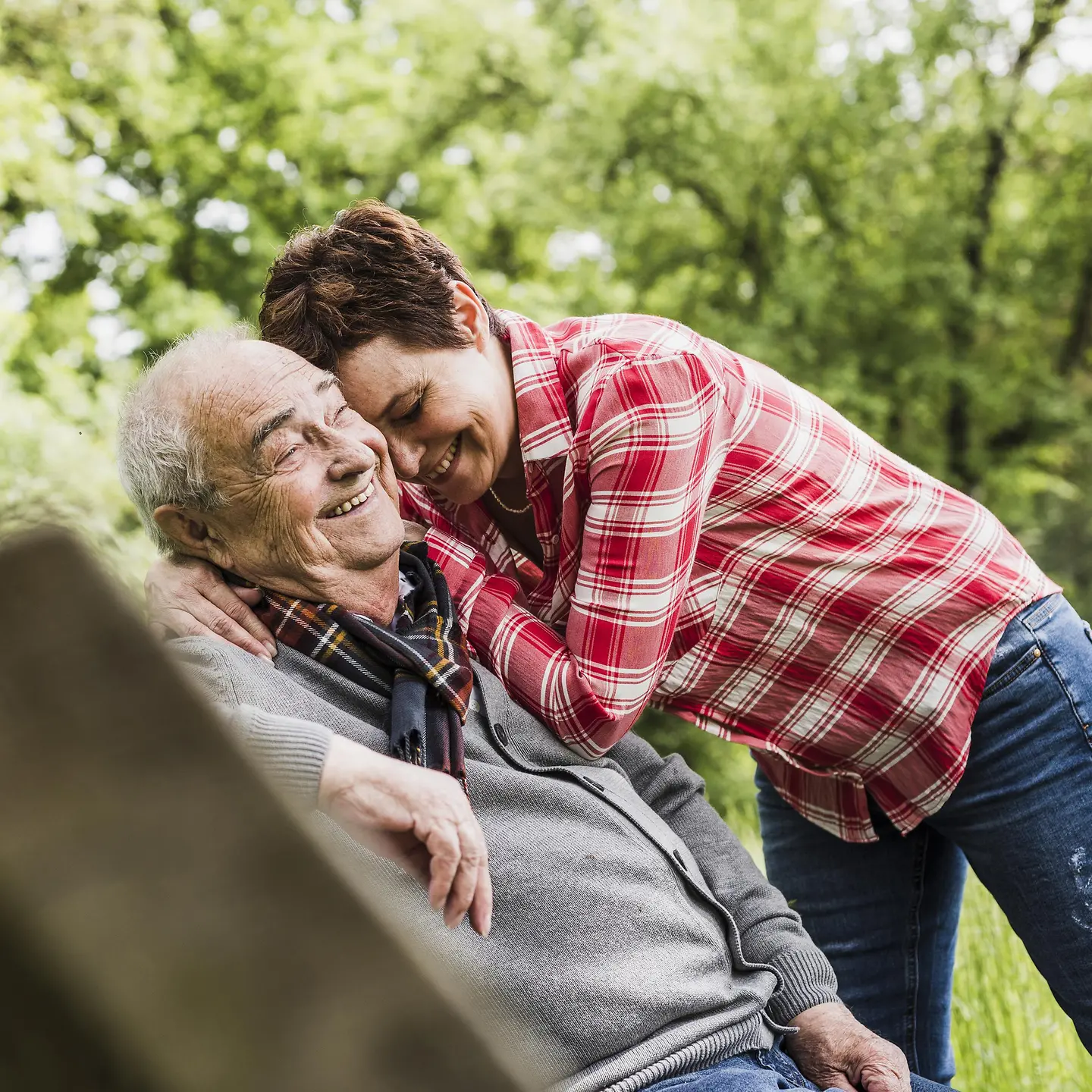 Eine Frau umarmt einen älteren Mann im Garten und beide lachen 