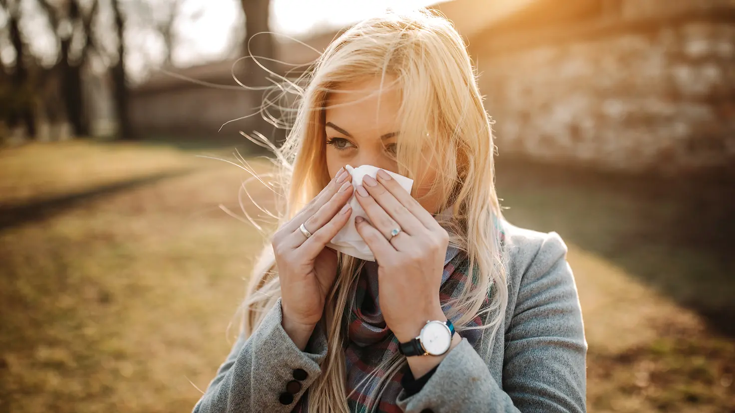 Eine junge Frau putzt sich mit einem Taschentuch die Nase.